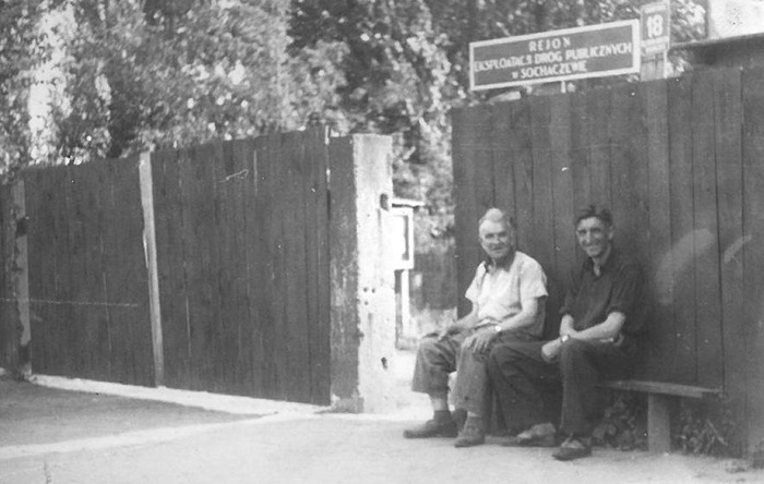 Dw&oacute;ch mężćzyzn siedzi na&nbsp;ławce, w&nbsp;tle drewniany płot. Fotografia czarno-biała