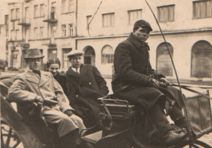 Zdjęcie przedstawia dwóch mężczyzn i kobietę jadących dorożką, na koźle siedzi dorożkarz