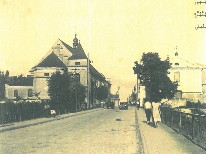 Zdjęcie przedstawia widok ulicy z&nbsp;kościołem po lewek stronie i&nbsp;klasztorem po prawej, chodnikiem ida kobiety