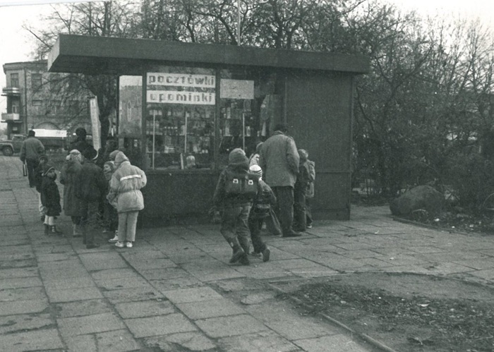 czarno-białe zdjęcie przedstawia grupę dzieci stojących przy kiosku