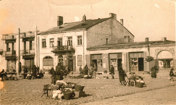 zdjęcie w kolorze sepii przedstawia brukowany rynek, na którym odbywa się handel i kamienice stojące w głębi